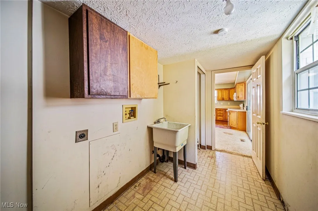 Washroom with brick patterned floors, cabinet space, hookup for an electric dryer, a textured ceiling, and washer hookup