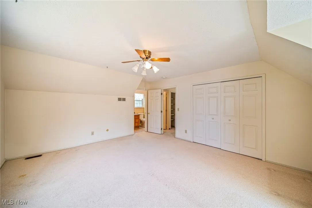 Unfurnished bedroom featuring lofted ceiling, carpet flooring, a closet, a ceiling fan, and ensuite bath