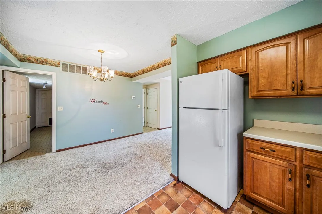 Kitchen with freestanding refrigerator, brown cabinets, light countertops, light carpet, and a textured ceiling