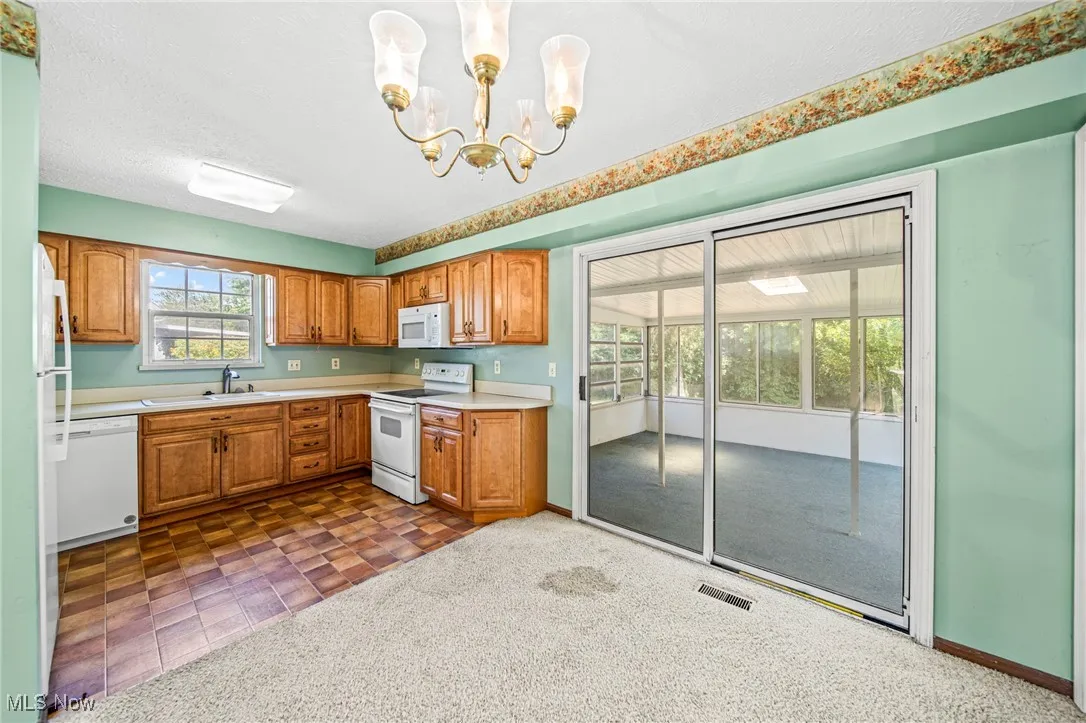 Kitchen featuring brown cabinetry, light countertops, white appliances, decorative light fixtures, and dark colored carpet