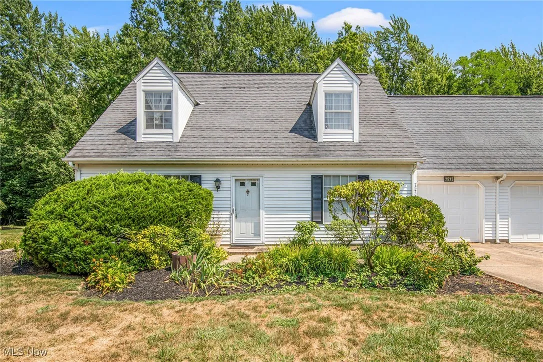 Cape cod home featuring an attached garage, driveway, a shingled roof, and a front yard