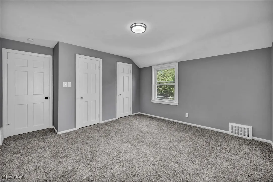 Unfurnished bedroom with two closets, carpet floors, and lofted ceiling
