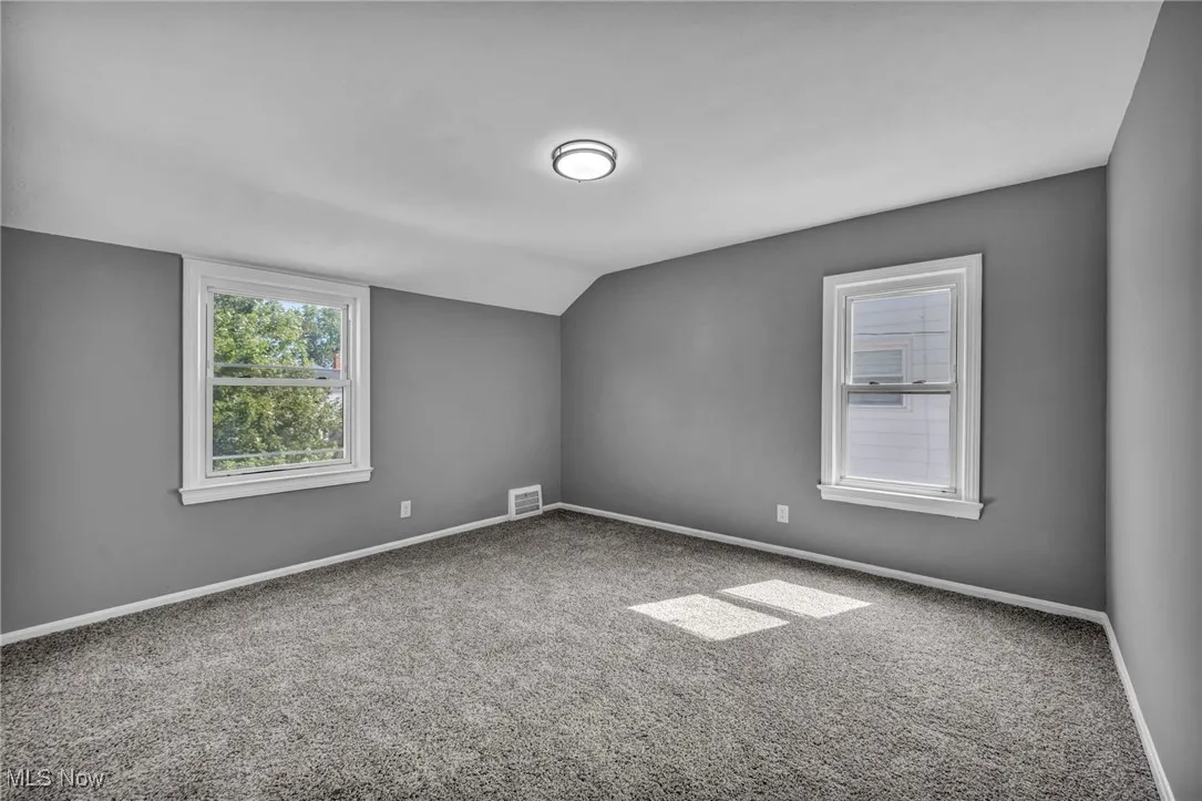 Carpeted spare room with baseboards and vaulted ceiling