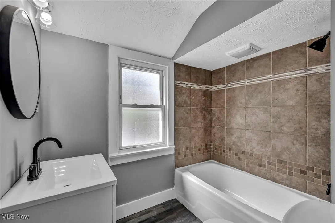 Bathroom with a textured ceiling, shower / washtub combination, vanity, and dark wood-style floors