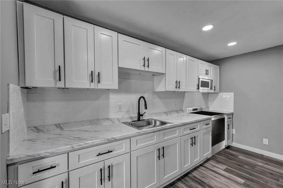 Kitchen with backsplash, appliances with stainless steel finishes, white cabinetry, recessed lighting, and dark wood-type flooring
