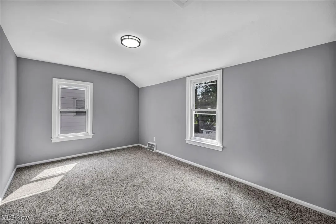 Carpeted spare room featuring baseboards and lofted ceiling