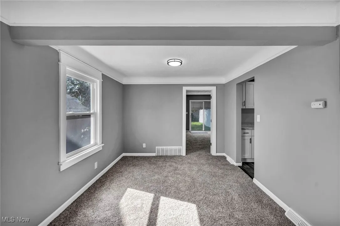 Spare room with dark colored carpet, healthy amount of natural light, and ornamental molding
