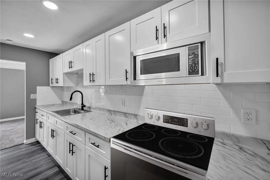 Kitchen featuring range with electric cooktop, backsplash, white cabinetry, stainless steel microwave, and dark wood-type flooring