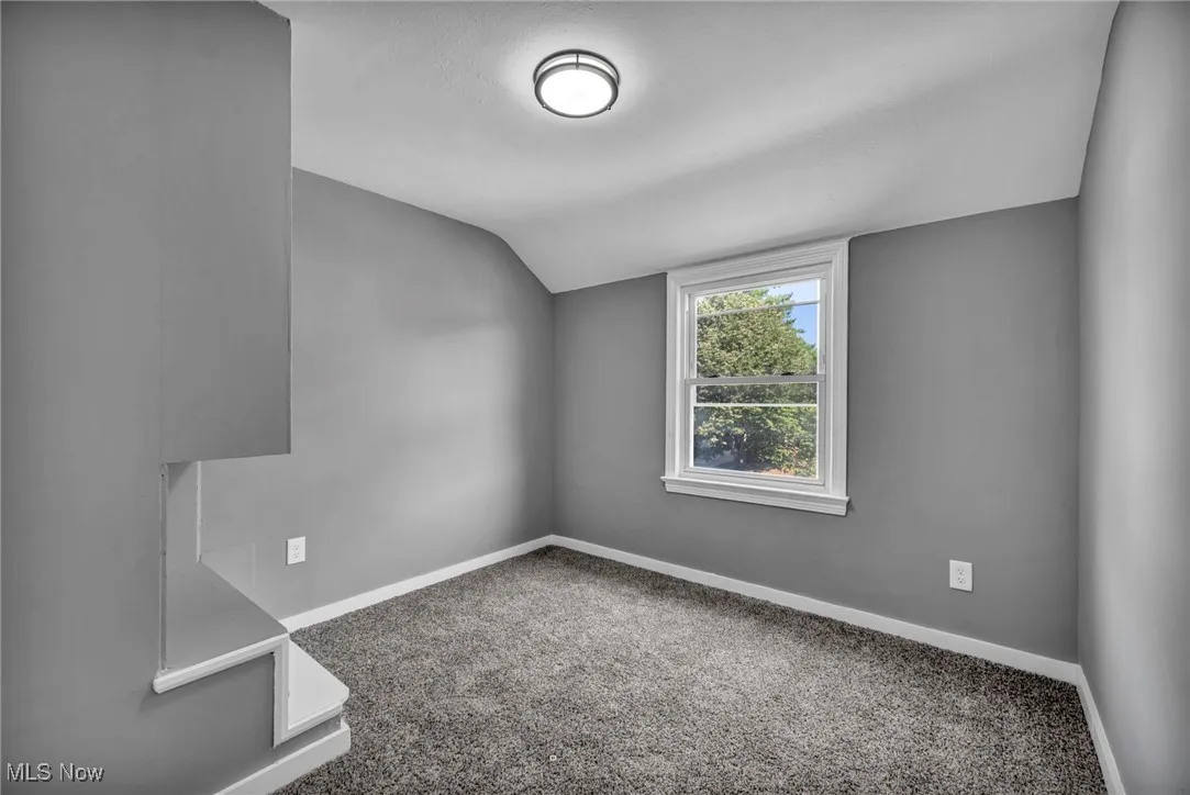 Carpeted spare room with baseboards and vaulted ceiling