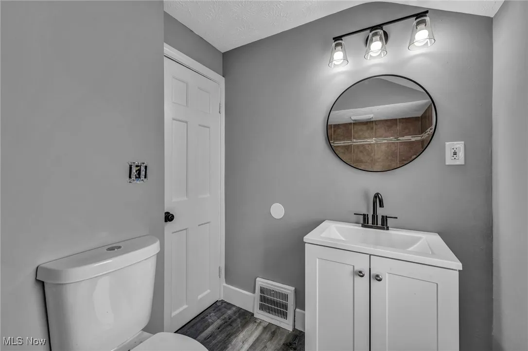 Half bath with vanity, a textured ceiling, and dark wood-style floors