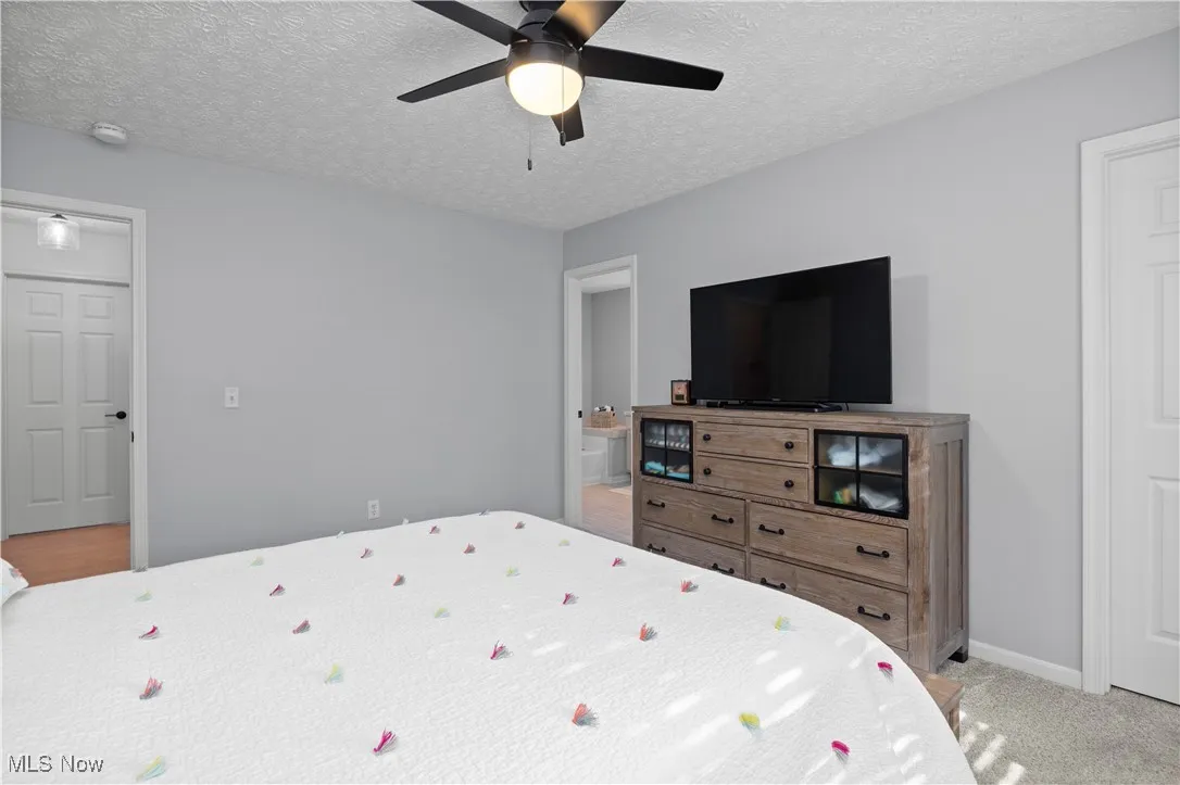 Bedroom with connected bathroom, a textured ceiling, ceiling fan, and light colored carpet