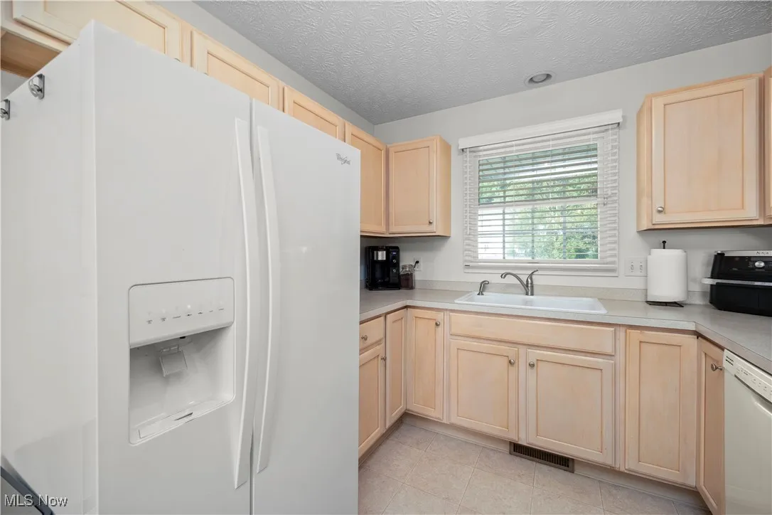 Kitchen featuring light brown cabinetry, white appliances, light countertops, a textured ceiling, and light tile patterned floors