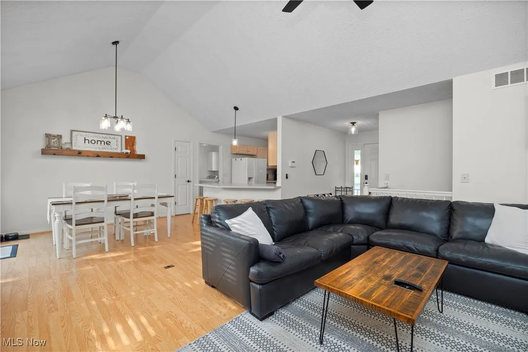 Living area featuring light wood-style flooring, ceiling fan, and high vaulted ceiling