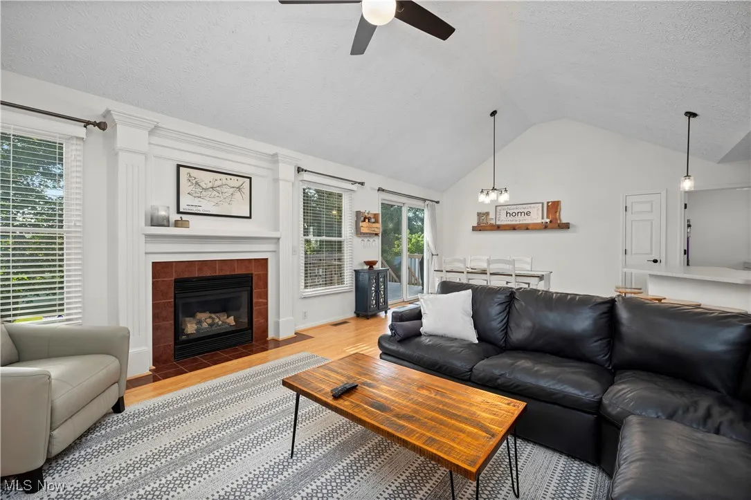 Living room with a textured ceiling, vaulted ceiling, wood finished floors, a tiled fireplace, and a chandelier