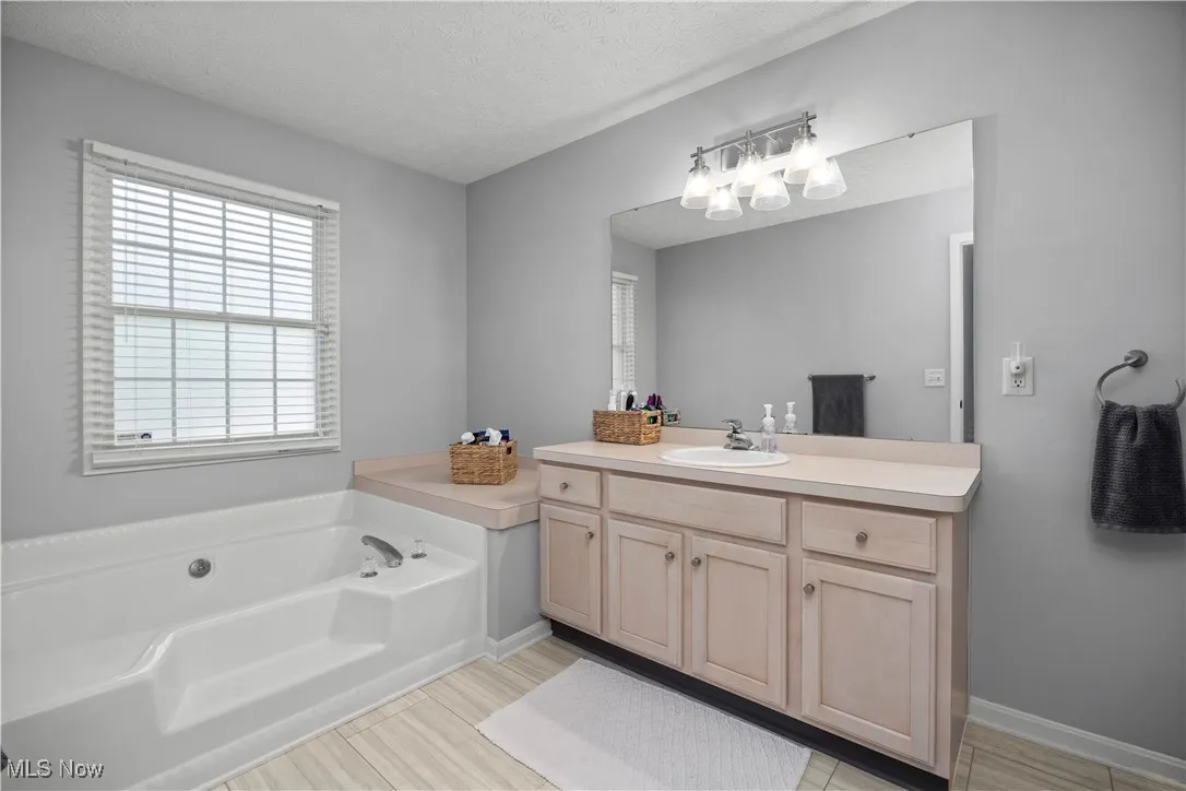 Bathroom featuring a textured ceiling, vanity, and a bath