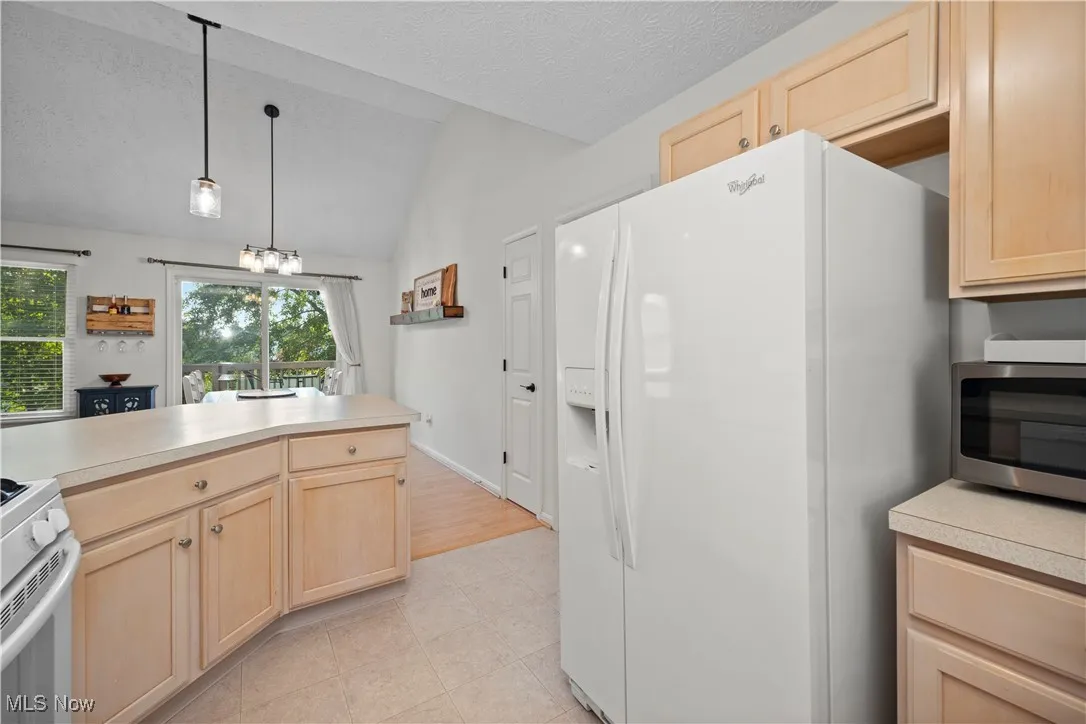Kitchen with light brown cabinets, white appliances, lofted ceiling, light countertops, and pendant lighting