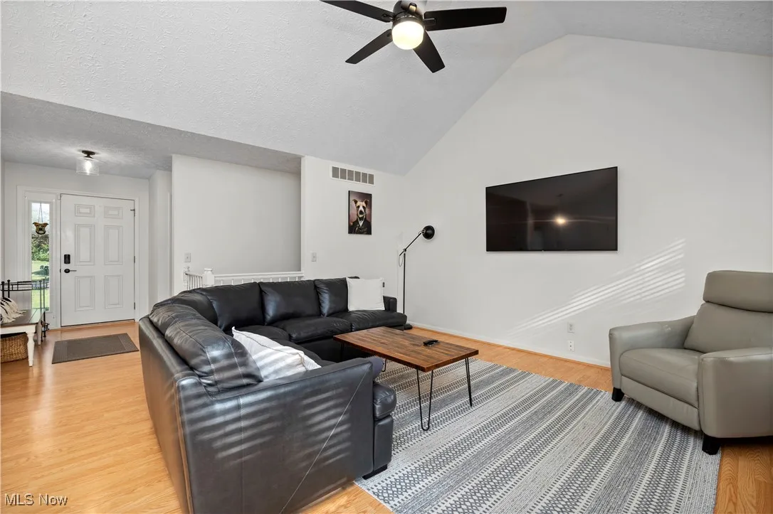 Living room featuring a textured ceiling, light wood-type flooring, vaulted ceiling, and ceiling fan