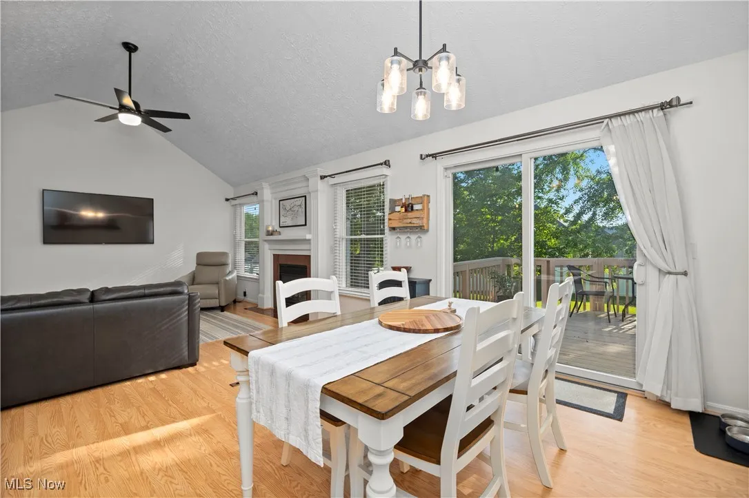 Dining room featuring vaulted ceiling, a textured ceiling, a fireplace, light wood-style floors, and a chandelier