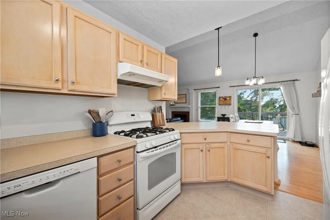 Kitchen featuring light brown cabinets, white appliances, light countertops, under cabinet range hood, and vaulted ceiling