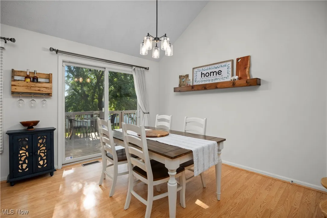 Dining area with light wood-style flooring, vaulted ceiling, and a chandelier