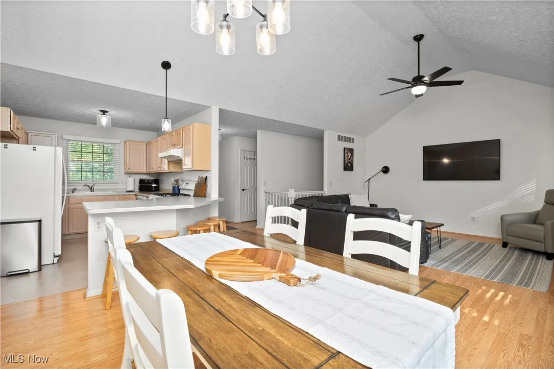 Dining space with a textured ceiling, a ceiling fan, light wood-style floors, vaulted ceiling, and a chandelier