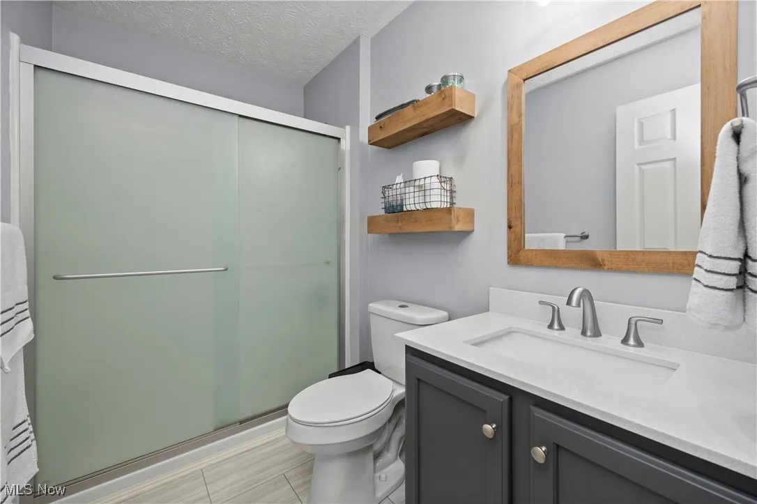 Full bathroom featuring a textured ceiling, vanity, and a stall shower