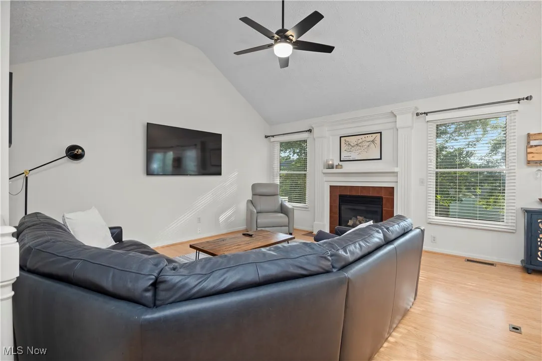 Living room featuring a tile fireplace, light wood-style floors, lofted ceiling, a textured ceiling, and a ceiling fan