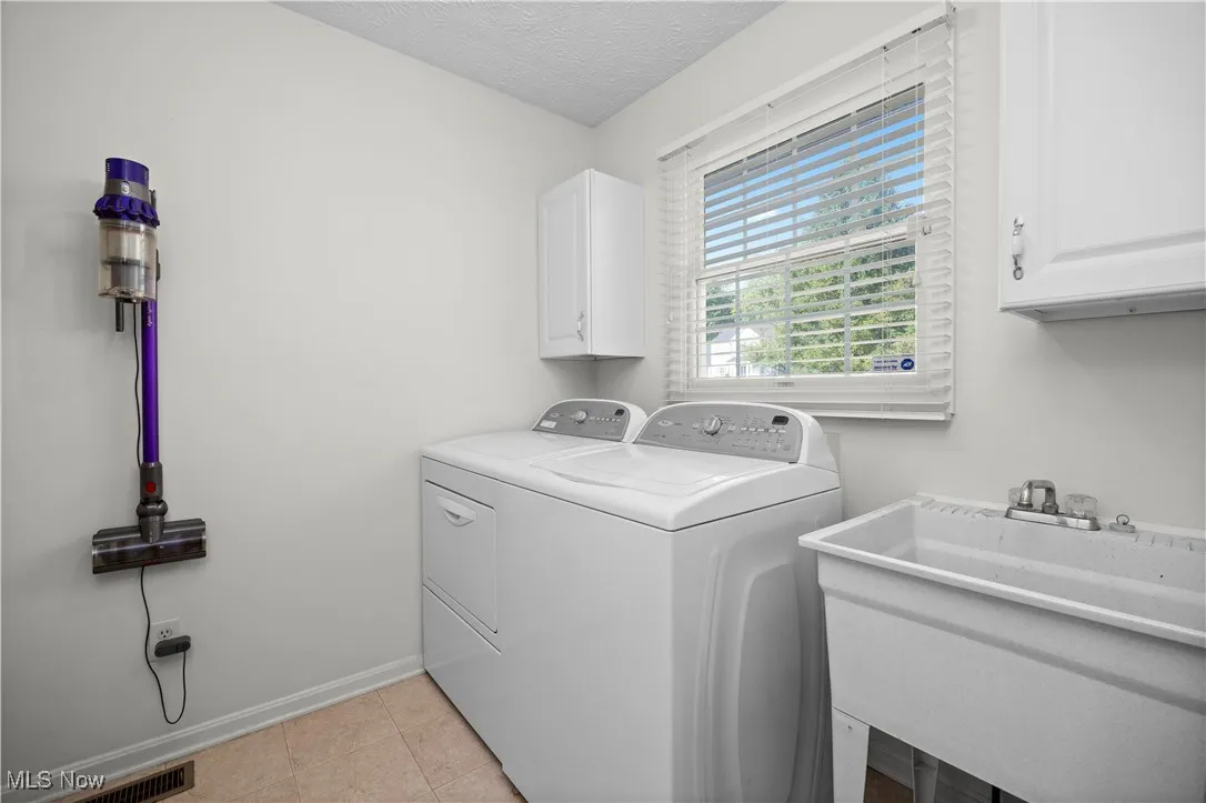 Washroom with cabinet space, a textured ceiling, washing machine and clothes dryer, and light tile patterned flooring