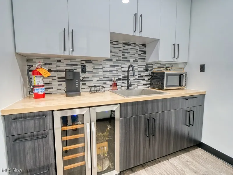 Bar area featuring gray cabinets, beverage cooler, backsplash, and light wood finished floors