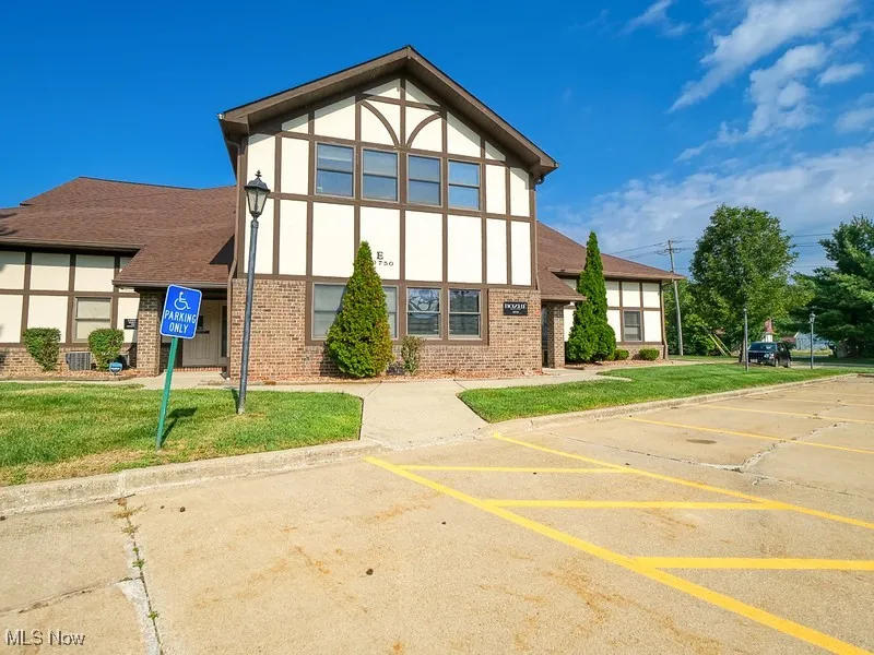 View of front of property featuring brick siding, a front lawn, stucco siding, and uncovered parking