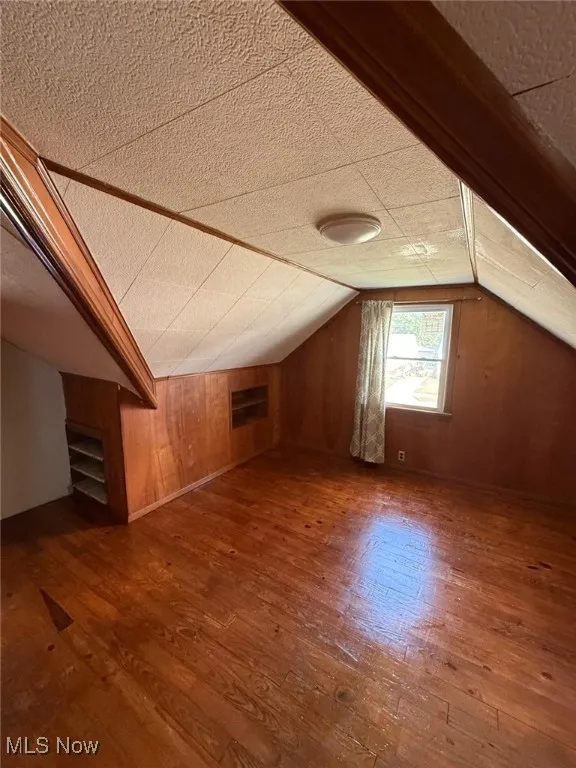 Additional living space with dark wood-style flooring, wood walls, and lofted ceiling