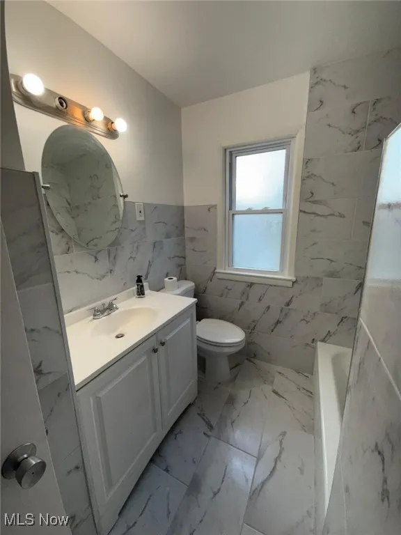 Full bathroom featuring tile walls, vanity, a wainscoted wall, and light marble finish floors