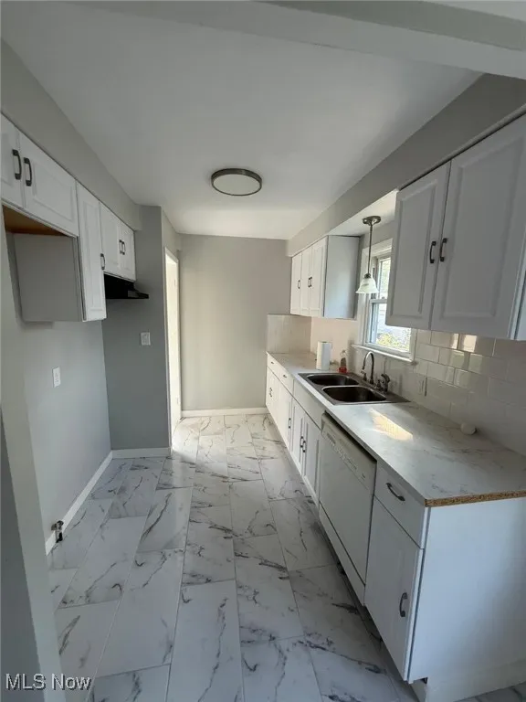 Kitchen with light countertops, white cabinetry, dishwasher, light marble finish flooring, and backsplash
