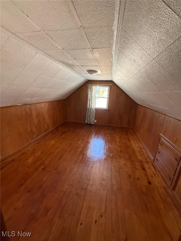 Additional living space with wood-type flooring, wood walls, and lofted ceiling