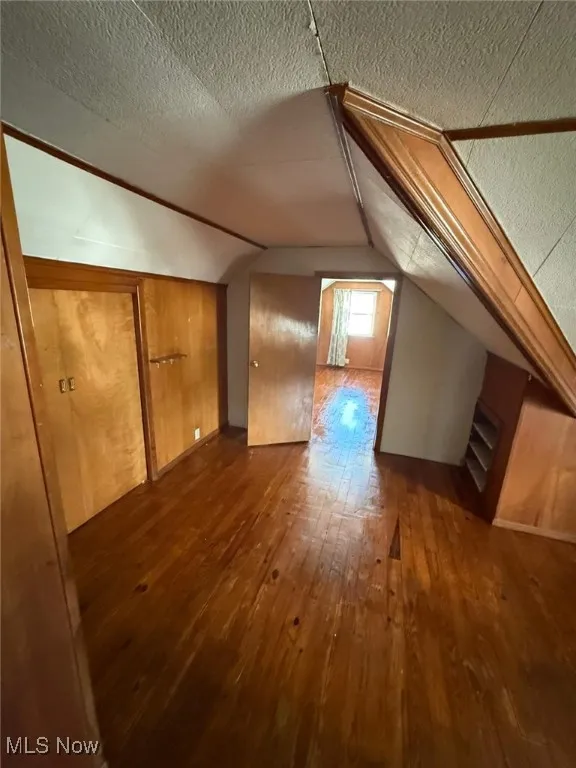 Additional living space featuring dark wood finished floors and vaulted ceiling