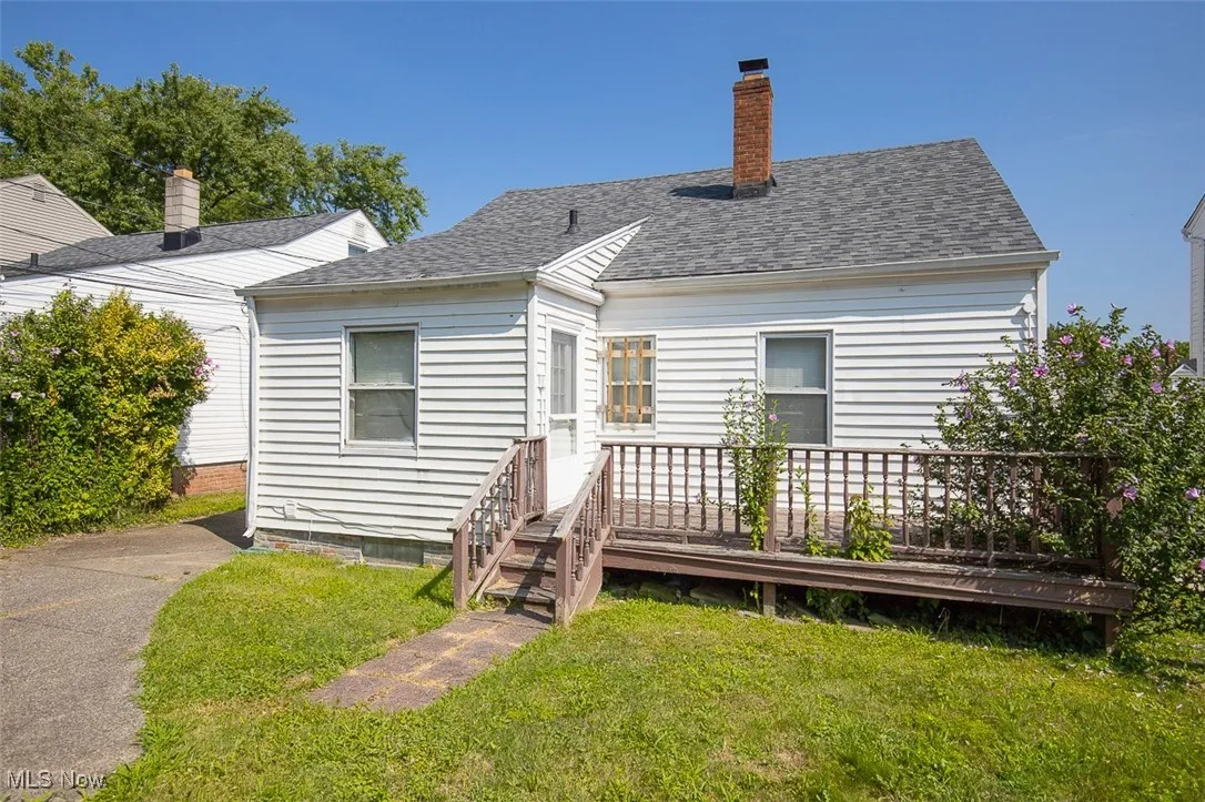 View of front of home featuring a deck, a front yard, roof with shingles, and a chimney