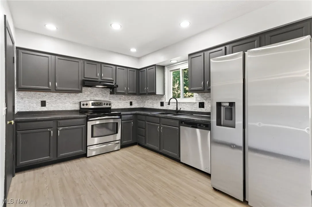 Kitchen featuring appliances with stainless steel finishes, dark countertops, decorative backsplash, light wood-type flooring, and recessed lighting