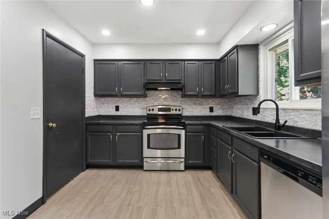 Kitchen featuring appliances with stainless steel finishes, light wood-type flooring, backsplash, recessed lighting, and under cabinet range hood