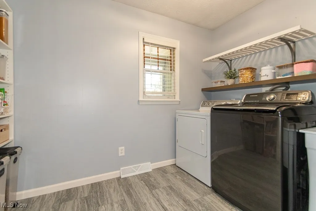 Laundry room with washing machine and dryer, light wood-type flooring, and a textured ceiling