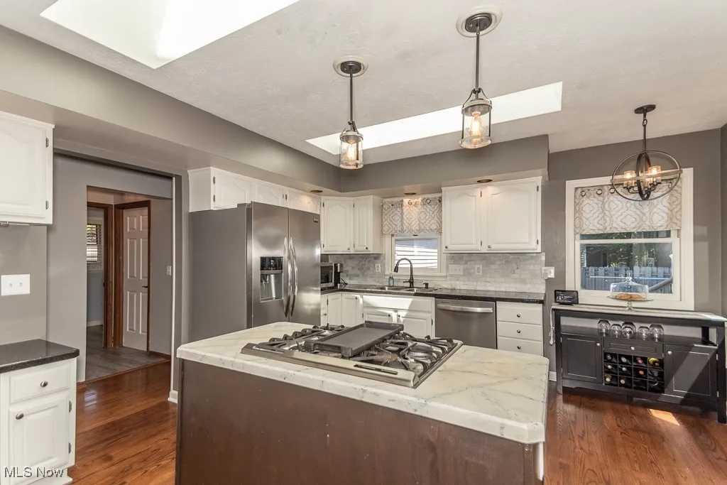 Kitchen with a kitchen island, a skylight, dark wood-type flooring, and white cabinets