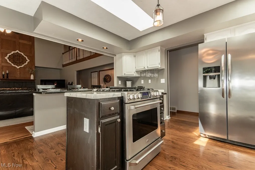Kitchen featuring stainless steel appliances, white cabinetry, dark wood-type flooring, open floor plan, and dark brown cabinetry
