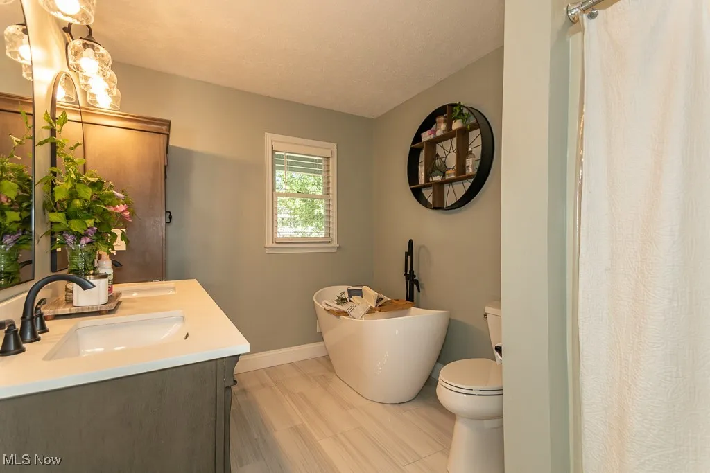 Full bath with a textured ceiling, a soaking tub, and double vanity
