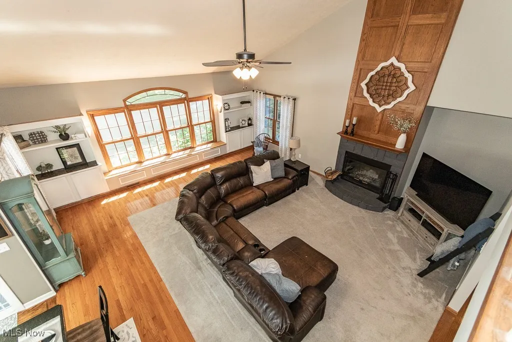 Living room featuring high vaulted ceiling, light wood-type flooring, a tiled fireplace, a ceiling fan, and built in shelves