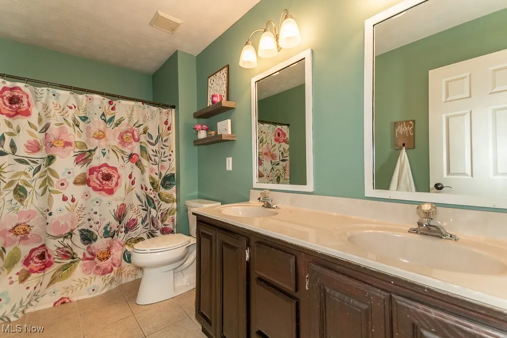 Bathroom with light tile patterned flooring, double vanity, a textured ceiling, and a shower with shower curtain