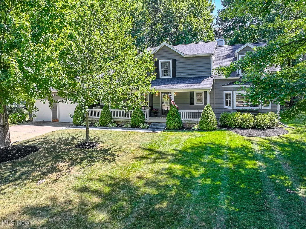 View of front of property with a porch, concrete driveway, a front lawn, a shingled roof, and a chimney