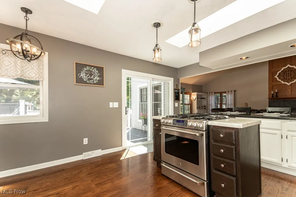 Kitchen featuring a skylight, stainless steel gas range oven, dark wood-style floors, white cabinetry, and healthy amount of natural light