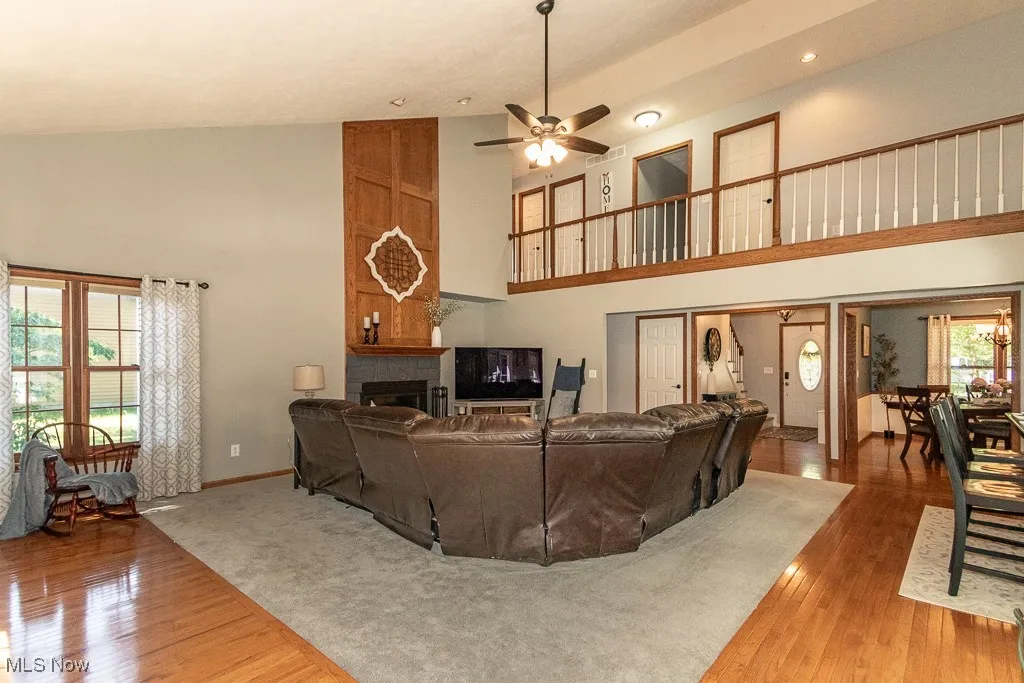 Living area featuring high vaulted ceiling, wood finished floors, a large fireplace, and ceiling fan