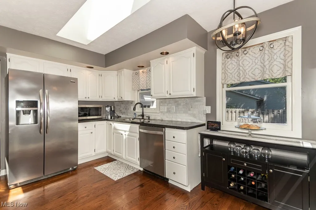 Kitchen with stainless steel appliances, white cabinets, dark wood-style flooring, backsplash, and a skylight