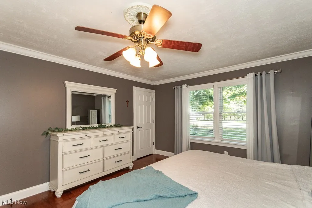 Bedroom with ornamental molding, dark wood-type flooring, and a ceiling fan