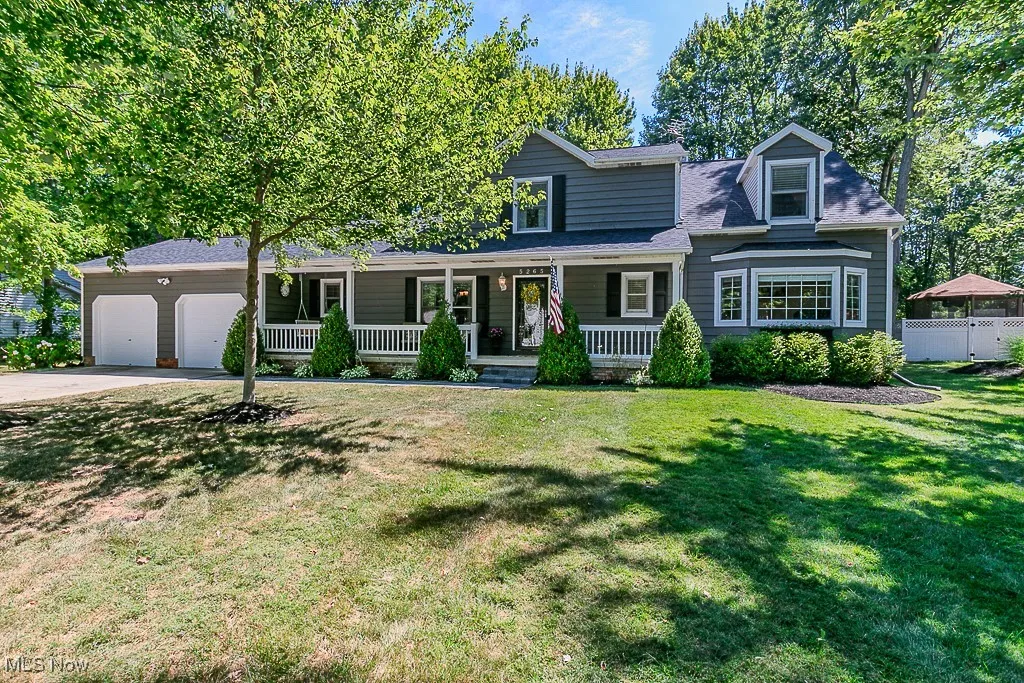 Traditional-style house featuring a porch, an attached garage, a front lawn, a shingled roof, and concrete driveway